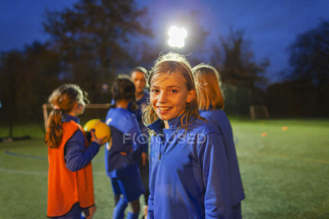 Portrait souriant, fille confiante joueur de football sur le terrain la nuit — Photo de stock