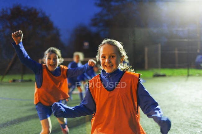 Portrait enthusiastic girl soccer players cheering on field at night — Stock Photo