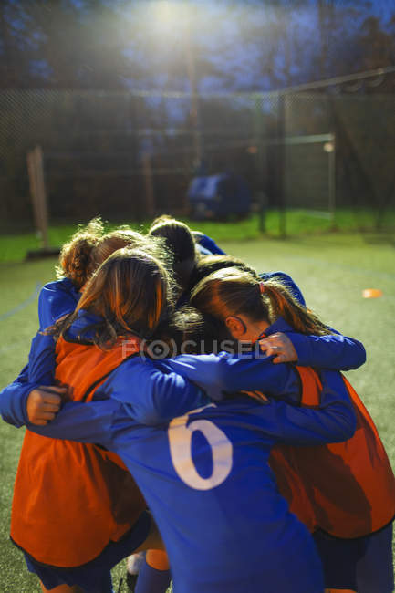 Girls soccer team in huddle on field at night — Stock Photo