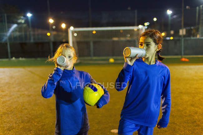 Girl soccer players taking a break, drinking water on field at night — Stock Photo
