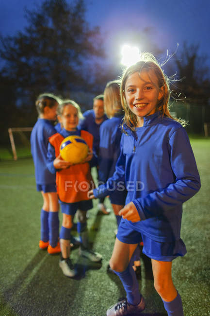 Portrait fille souriante et confiante footballeuse pratiquant avec l'équipe sur le terrain la nuit — Photo de stock