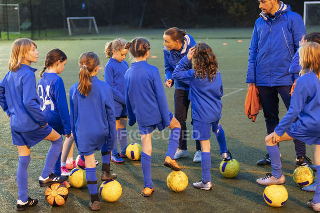 Girls soccer team listening to coaches on field — Stock Photo