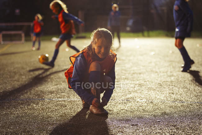 Ritratto sorridente ragazza calciatore legatura scarpa sul campo di notte — Foto stock