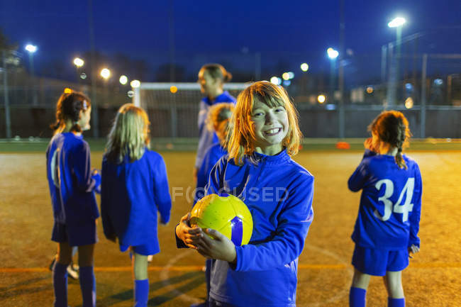 Retrato sorridente, menina entusiasmada desfrutando de prática de futebol em campo à noite — Fotografia de Stock