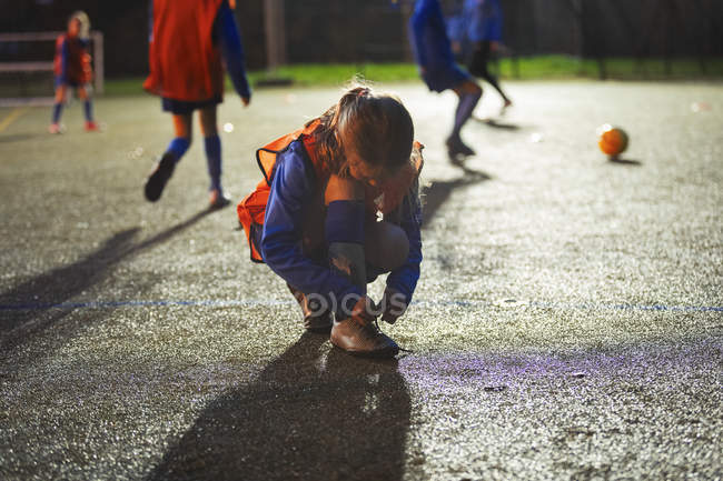 Chica futbolista atando zapato en el campo por la noche - foto de stock