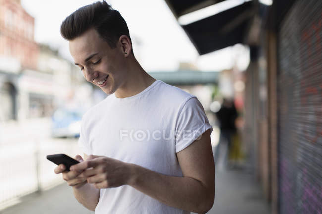 Усміхнений хлопчик-підліток використовує смартфон на міському тротуарі — стокове фото