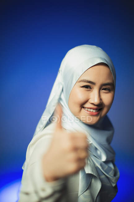 Портрет улыбается, уверенная в себе молодая женщина в синем шелковом хиджабе жестом вверх — стоковое фото