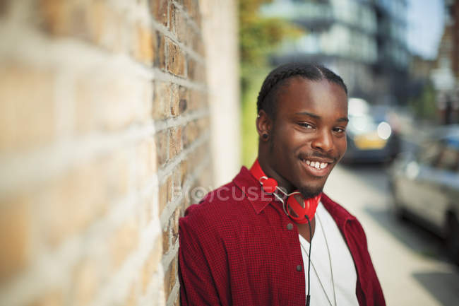 Retrato sonriente, adolescente confiado con auriculares en la acera urbana - foto de stock