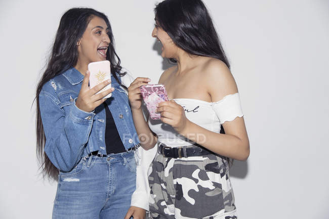Laughing teenage twin sisters using smart phones — Stock Photo
