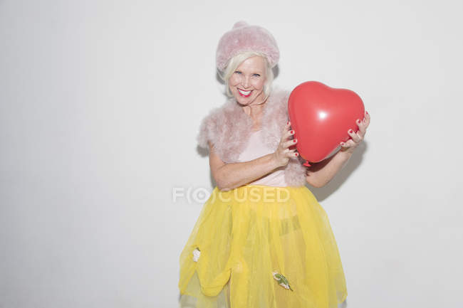 Портрет усміхнений, впевнена старша жінка тримає повітряну кулю у формі серця — стокове фото