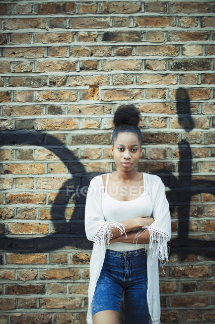 Portrait confiant, jeune femme sérieuse appuyé contre un mur de briques — Photo de stock