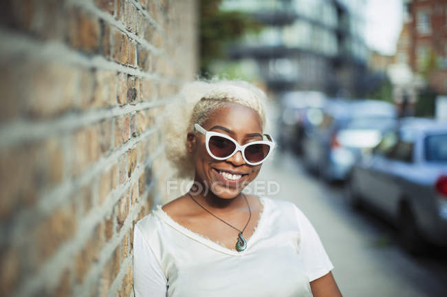 Portrait jeune femme souriante et confiante en lunettes de soleil sur le trottoir urbain — Photo de stock