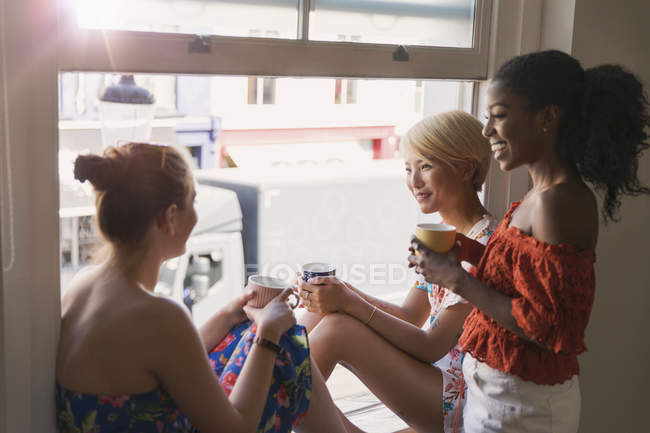 Jóvenes amigas tomando té en la ventana del apartamento - foto de stock