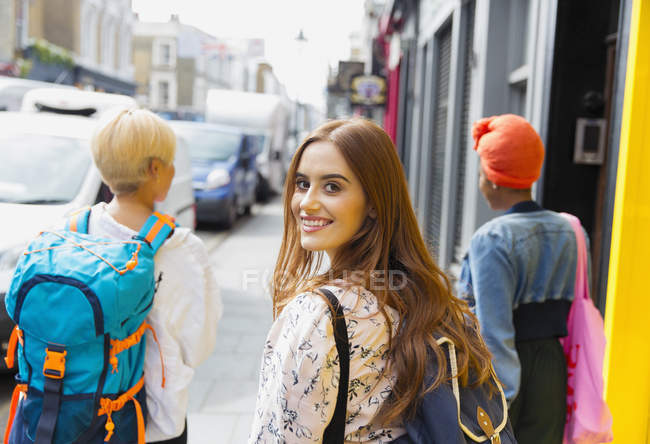 Портрет улыбающейся, уверенной молодой женщины с рюкзаком на городском тротуаре — стоковое фото