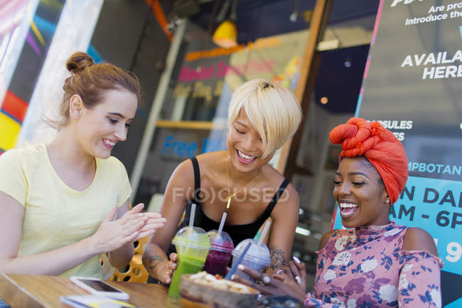 Молоді жінки друзі насолоджуються коктейлями в тротуарному кафе — стокове фото