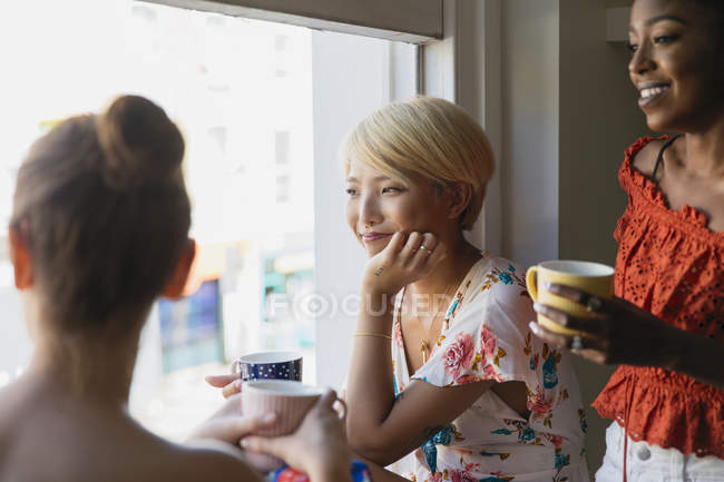 Jóvenes amigas tomando café en la ventana del apartamento - foto de stock