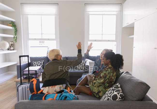 Young women friends with suitcases high-fiving in living room — Stock Photo