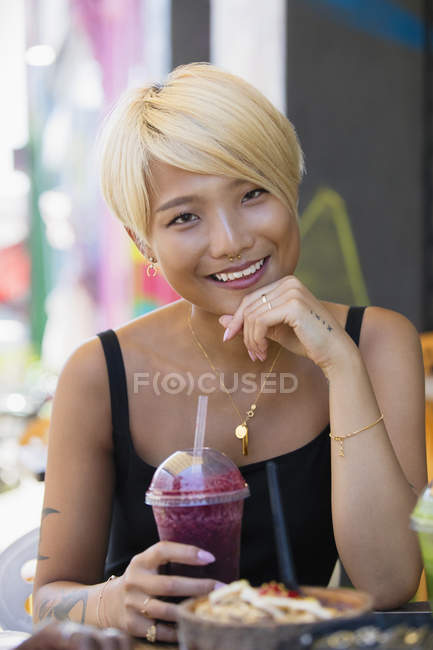 Портрет усміхнений, впевнена молода жінка п'є смузі в тротуарному кафе — стокове фото
