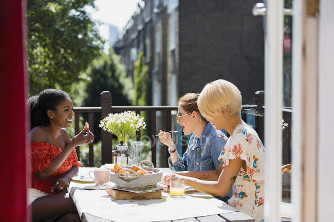 Mujeres jóvenes amigas comiendo almuerzo en el balcón del apartamento soleado - foto de stock