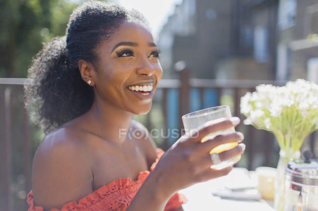 Happy young woman drinking orange juice on sunny balcony — Stock Photo