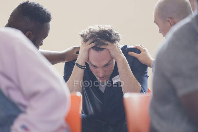 Hombres reconfortante molesto hombre en terapia de grupo - foto de stock