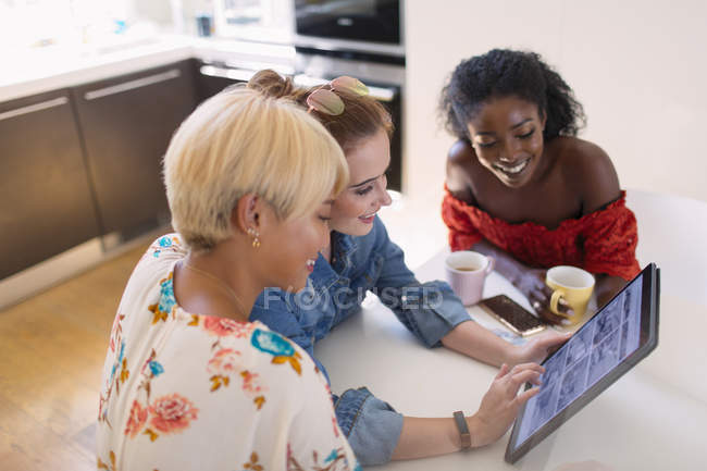 Young women friends using digital tablet at kitchen table — Stock Photo