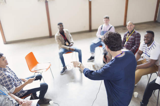 Человек с микрофоном разговаривает с мужчинами в групповой терапии — стоковое фото