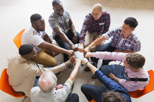 Мужчины, соединяющие кулаки в круг в групповой терапии — стоковое фото