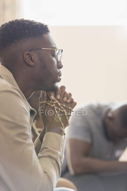 Jovem sereno rezando com rosário em grupo de oração — Fotografia de Stock