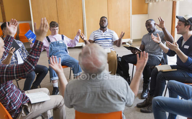Hombres rezando con los brazos levantados en grupo de oración - foto de stock