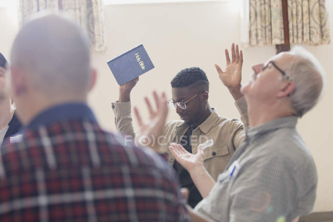 Men with bible praying with arms raised in prayer group — Stock Photo