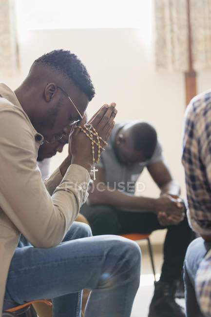 Serene man praying with rosary in prayer group — Stock Photo