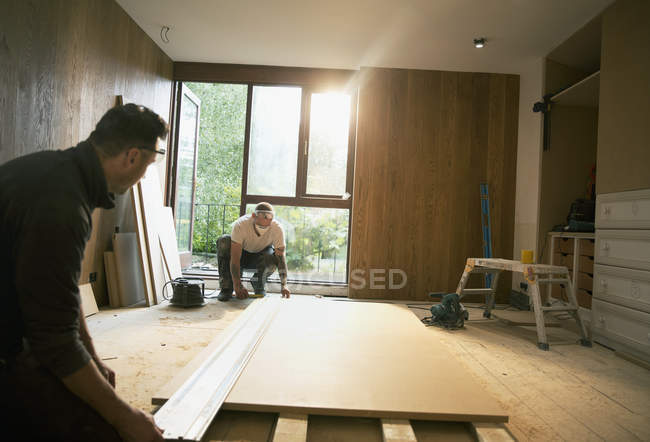 Trabalhadores da construção civil que medem placa de madeira em casa — Fotografia de Stock