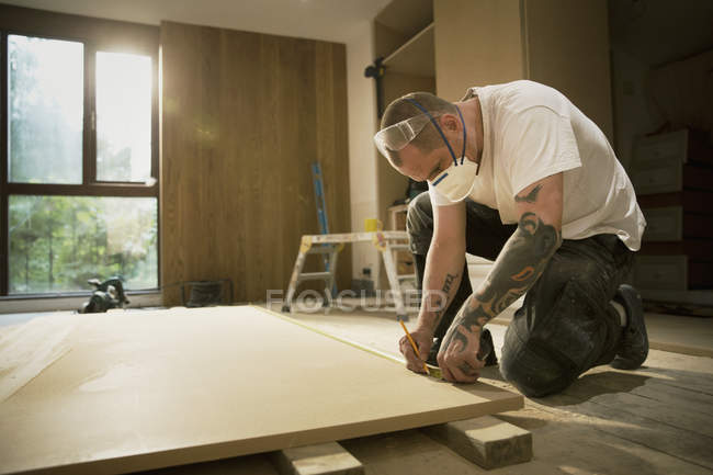Trabalhador da construção com tatuagens que medem e marcam a placa de madeira em casa — Fotografia de Stock