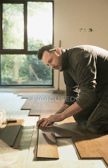 Travailleur de la construction concentré pose de planchers de bois franc dans la maison — Photo de stock