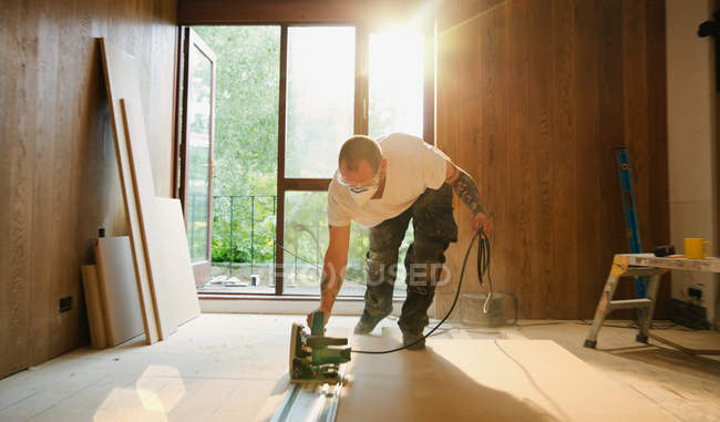 Trabalhador da construção civil usando serra elétrica para cortar madeira em casa — Fotografia de Stock