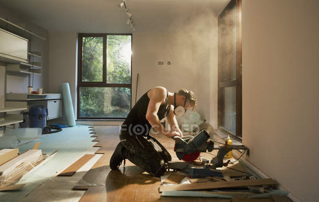 Trabalhador da construção civil usando serra elétrica para cortar piso de madeira em casa — Fotografia de Stock