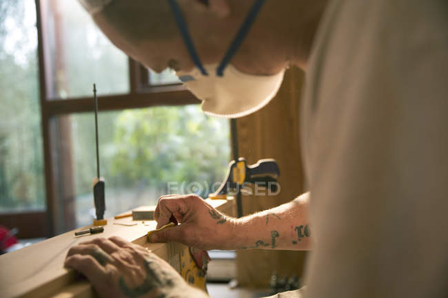 Закрыть строителя татуировками, осматривая деревянную доску — стоковое фото