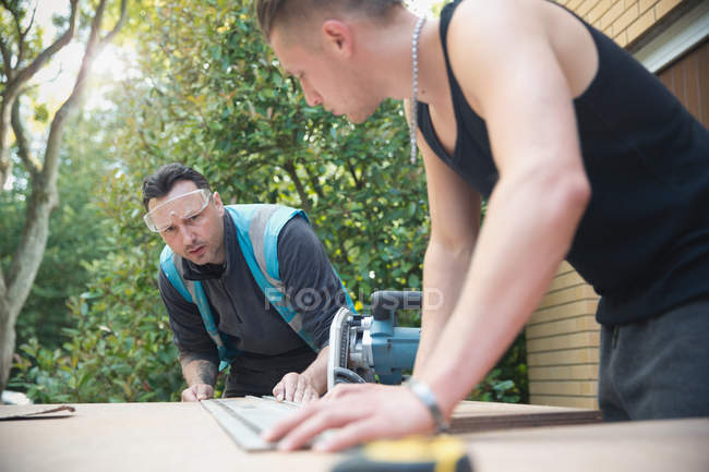 Construction workers measuring wood in driveway — Stock Photo