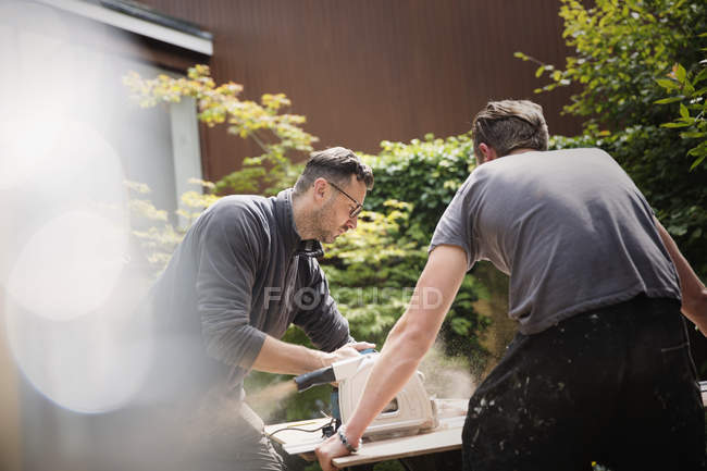 Construction workers using table saw to cut wood in driveway — Stock Photo