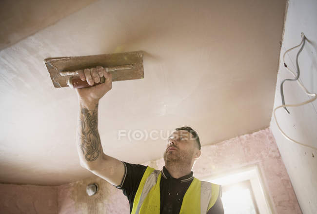 Construction worker with tattoo plastering ceiling — Stock Photo