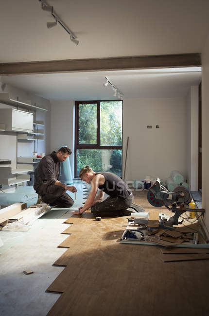 Trabalhadores da construção civil que colocam piso de madeira em casa — Fotografia de Stock