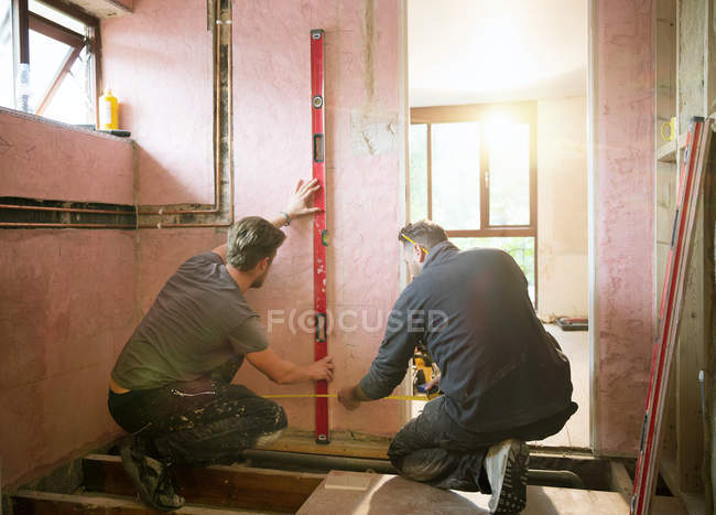 Travailleurs de la construction utilisant l'outil de niveau et le ruban à mesurer dans la maison — Photo de stock