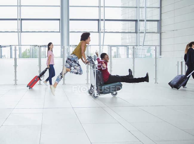 Playful couple pushing luggage cart in airport — Stock Photo