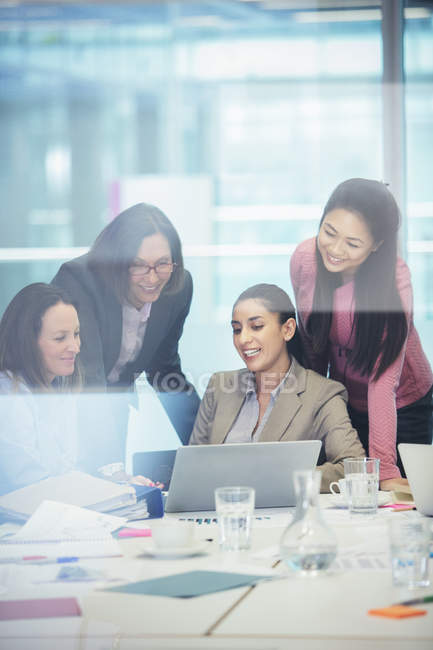 Mujeres de negocios sonrientes usando laptop en reunión de sala de conferencias - foto de stock