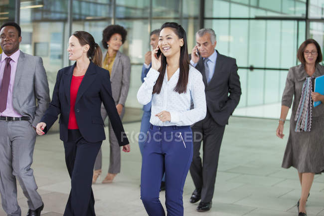 Mujer de negocios sonriente hablando por teléfono celular y caminando - foto de stock