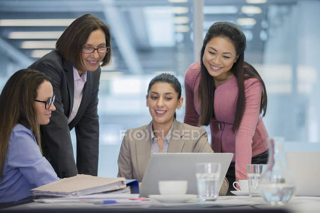 Mujeres de negocios sonrientes usando laptop en reunión de sala de conferencias - foto de stock