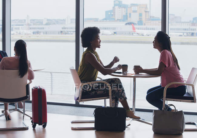 Empresarias hablando y tomando café en la sala de negocios del aeropuerto - foto de stock