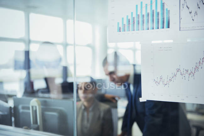 Business people using computer behind charts and graphs in office — Stock Photo