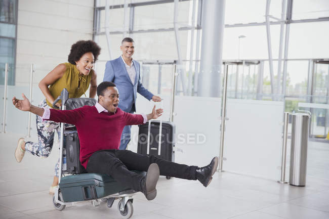 Verspieltes Paar läuft mit Gepäckwagen in Flughafen — Stockfoto